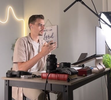 Tabor Normoyle speaking beside a desk with camera equipment and a laptop